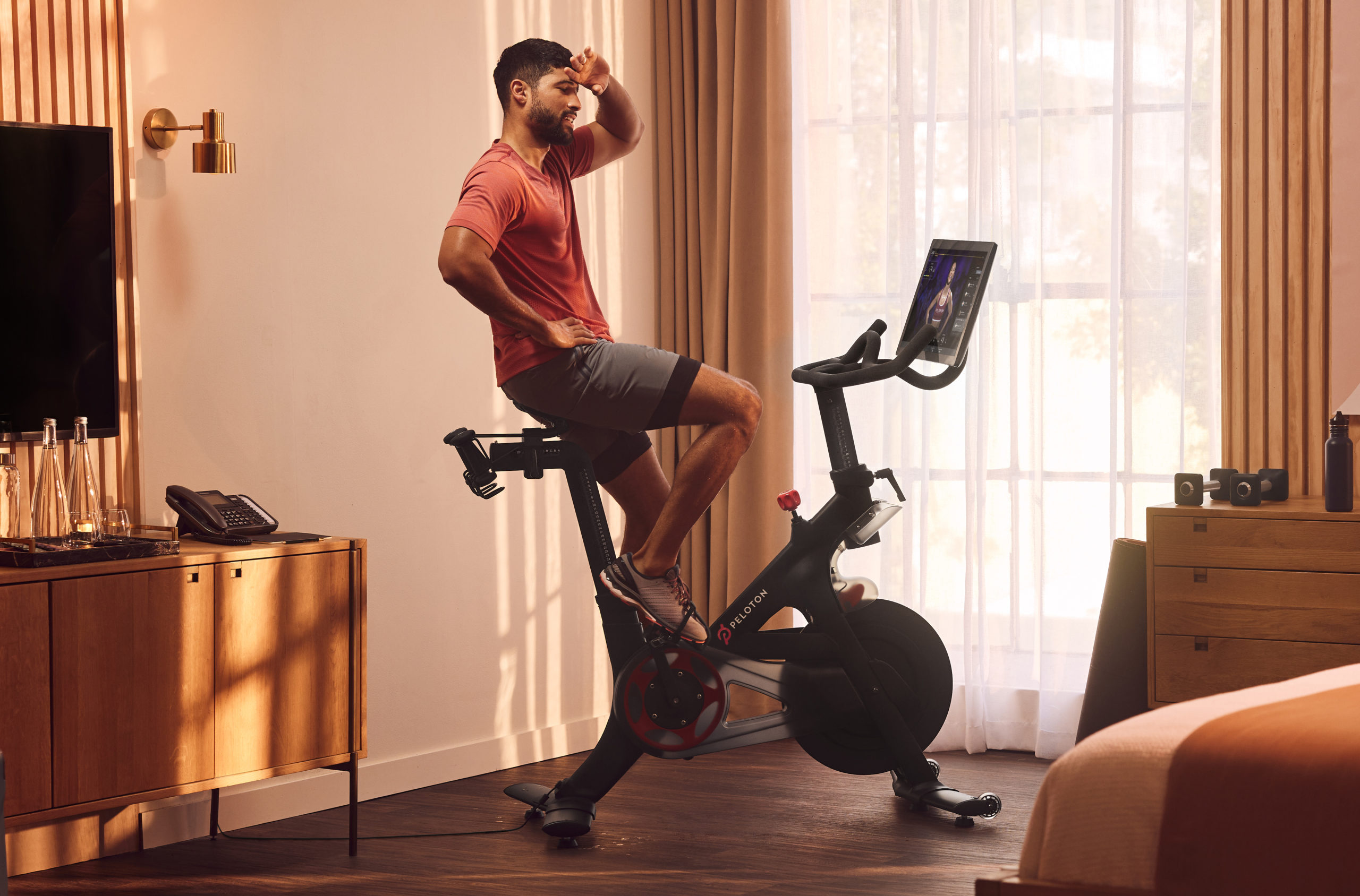 man riding a peloton bike in a bedroom or hotel